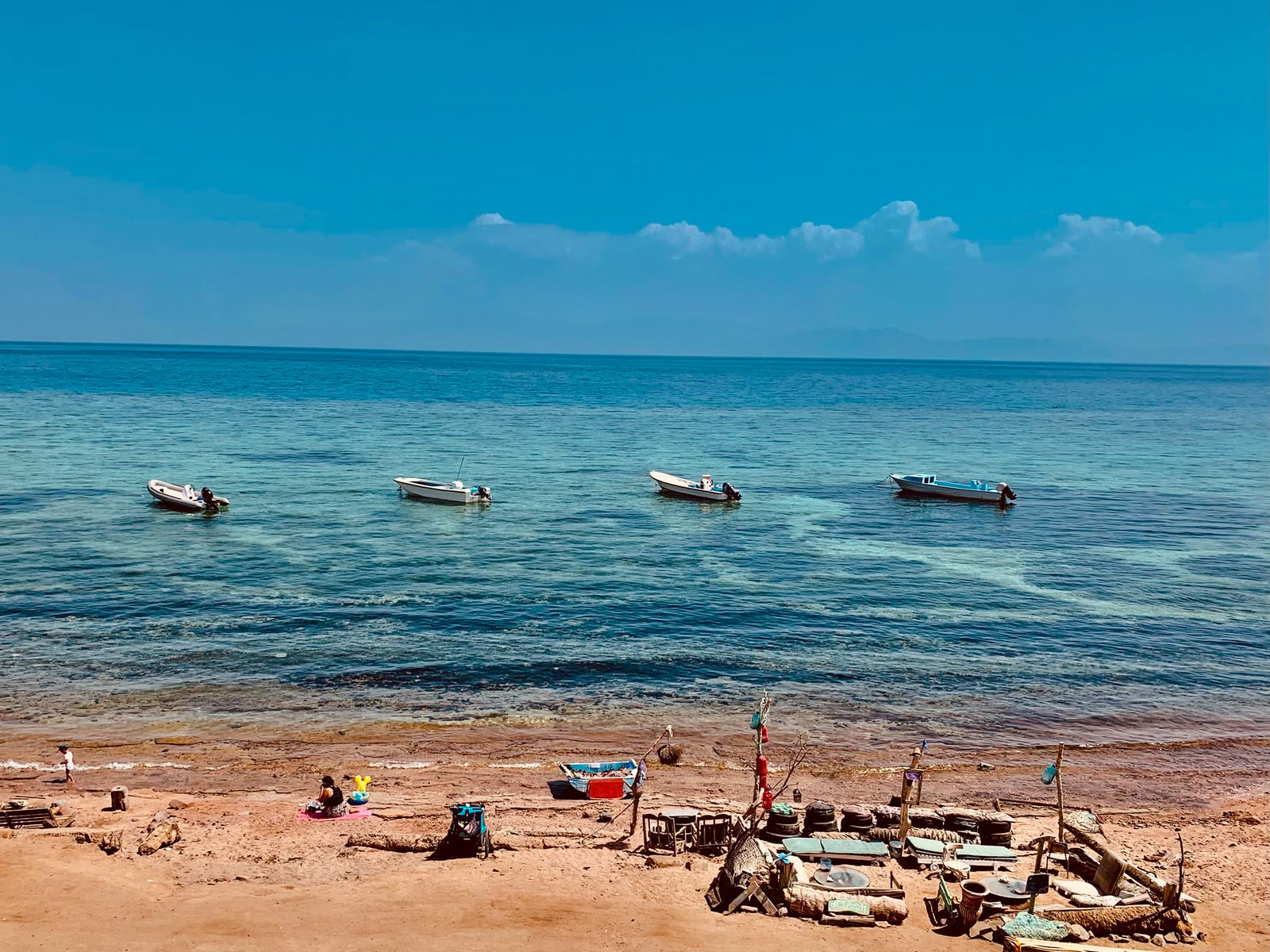 Small boats moored off a sandy beach, the Gulf of Aqaba beyond.