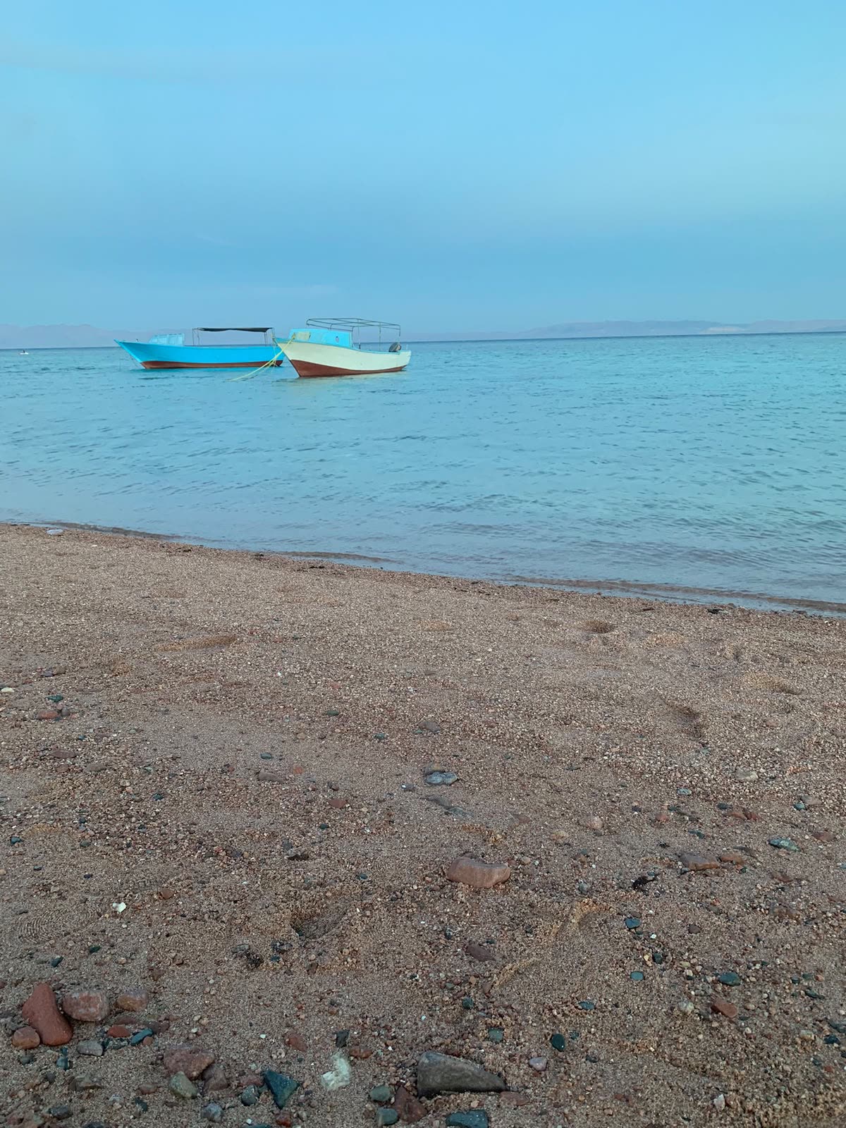 Two small boats on calm, shallow water off a quiet beach.
