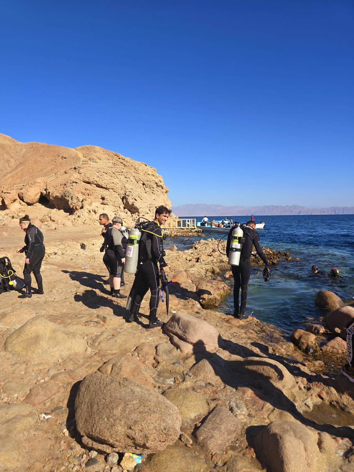 Divers in full kit crossing the rocks to a shore entry.