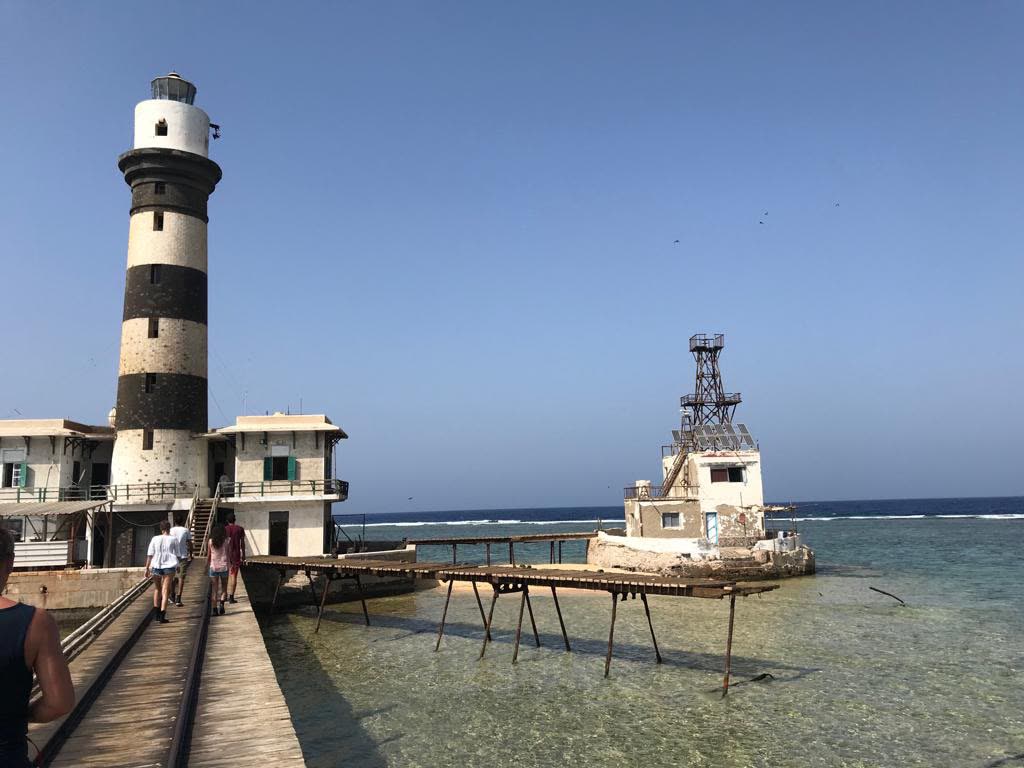 A striped lighthouse at the end of a wooden jetty over shallow reef.