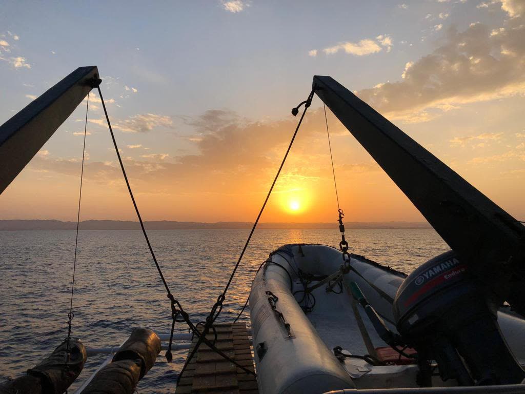 The tender hanging from its davits at sunset, the sea flat and gold.
