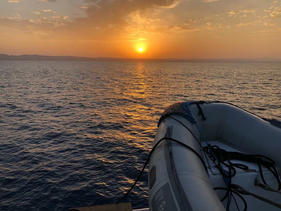 The sun setting over calm sea, seen past the tender on the back of the boat.