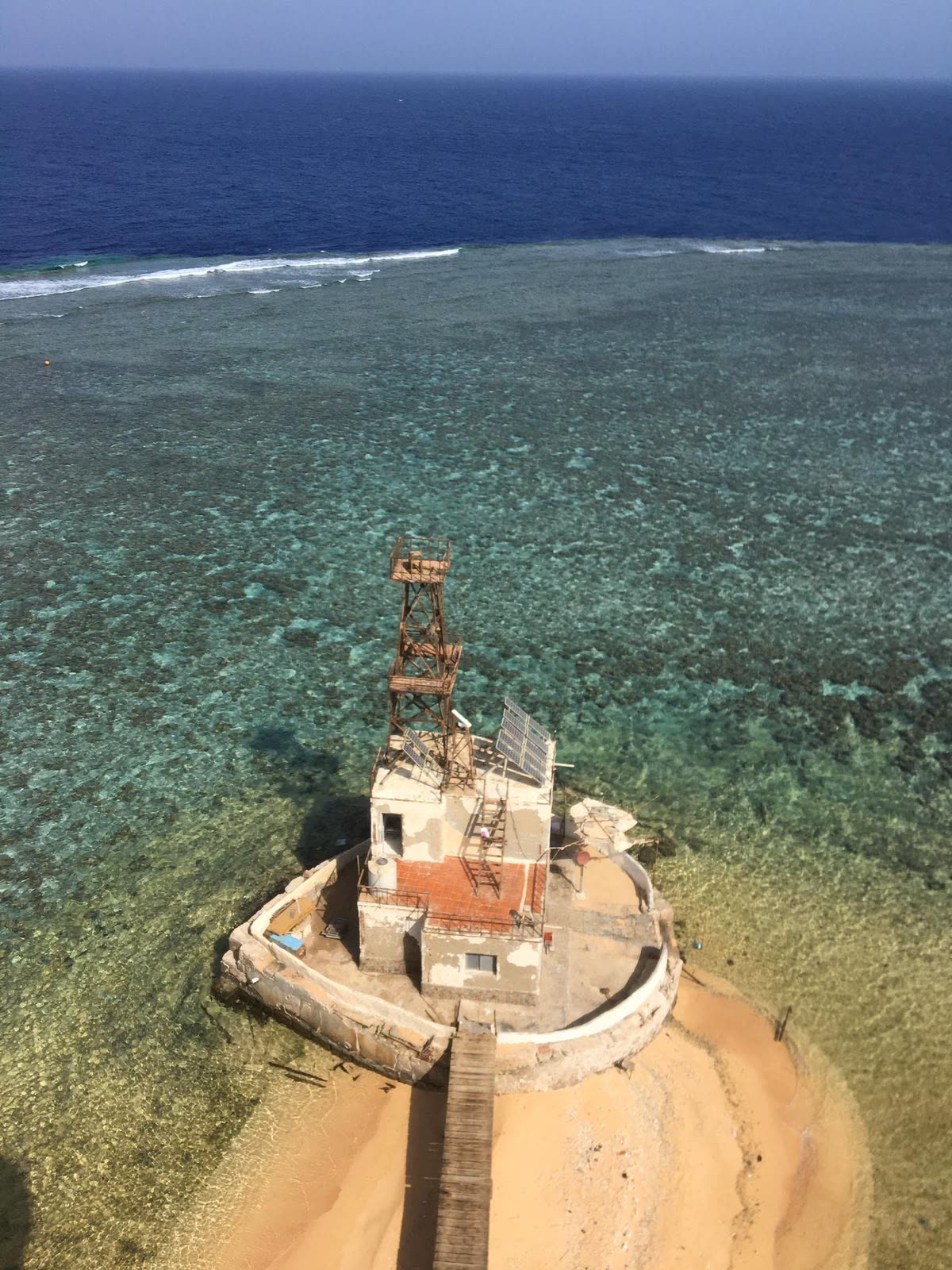 An old tower and building standing on the reef, clear shallow water all around.