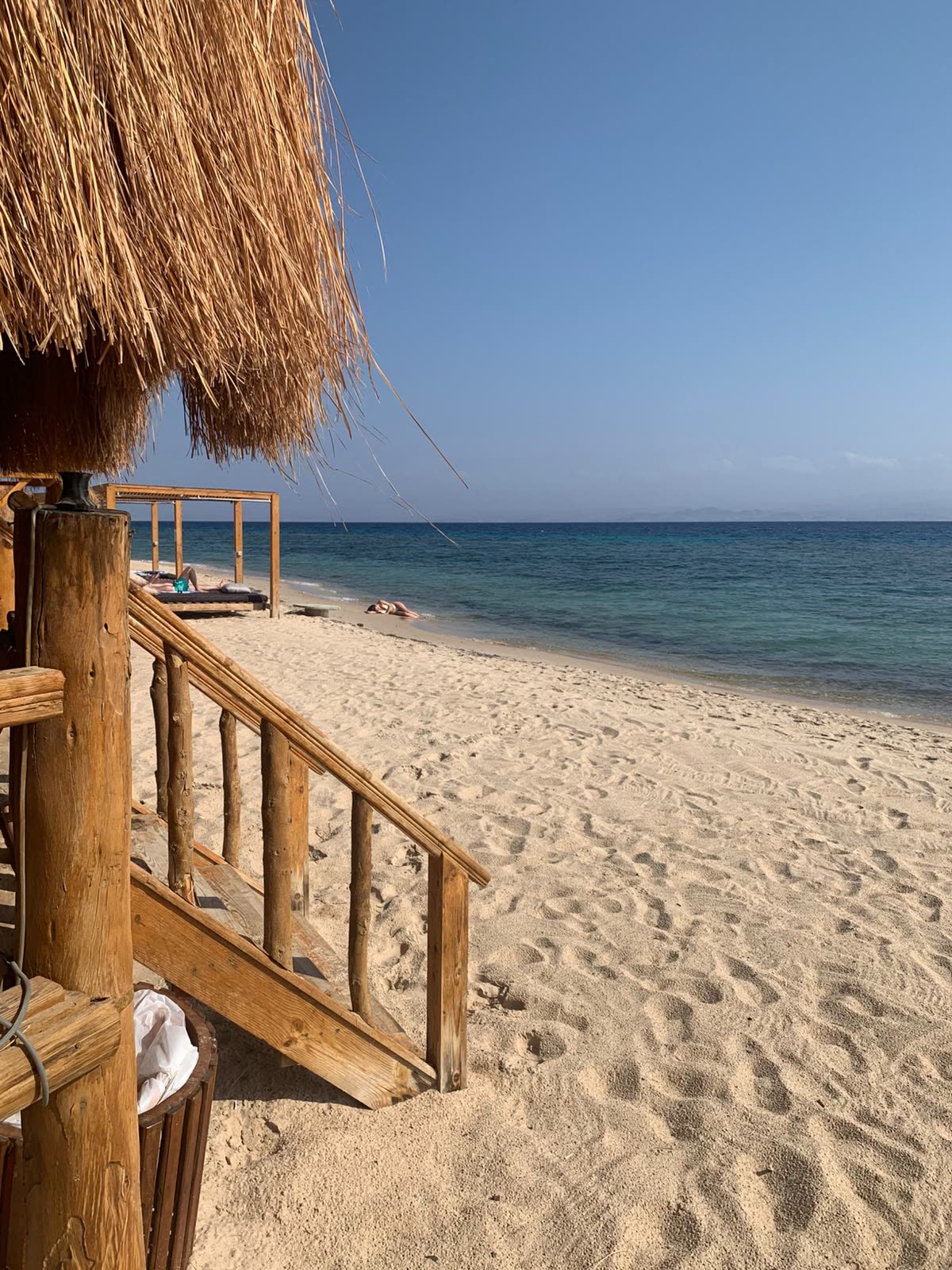 A wooden stair leading down from a palm thatched shade to an empty white beach.