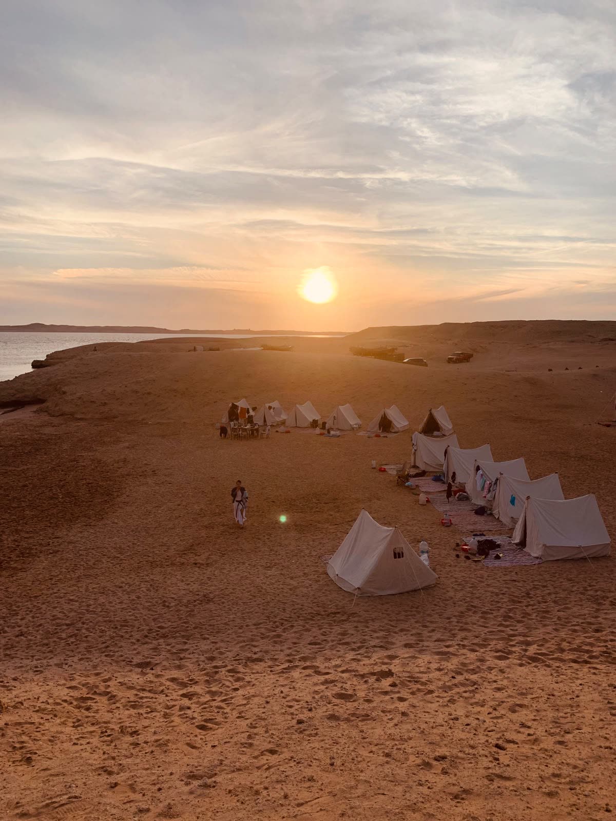 The camp seen from a dune at sunset, a circle of white tents on the sand.