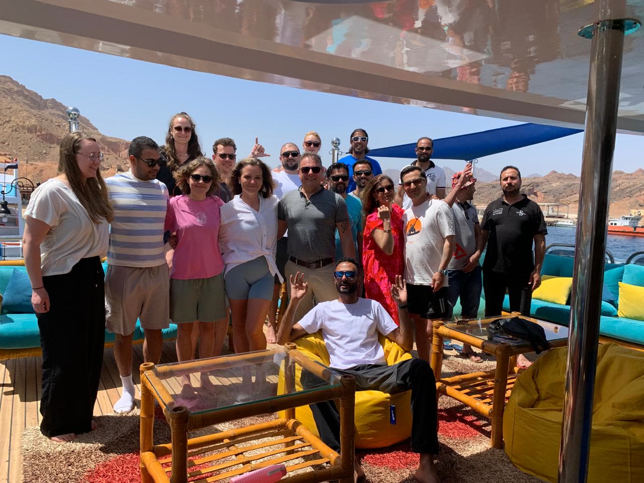 A big group of divers and crew posing together on the shaded upper deck of a boat.