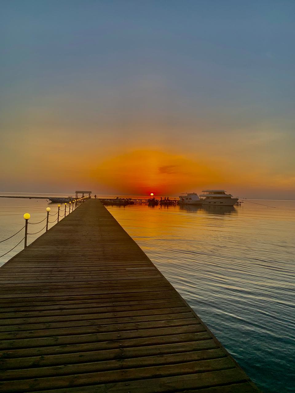 A wooden jetty running out toward the setting sun, boats moored at the far end.