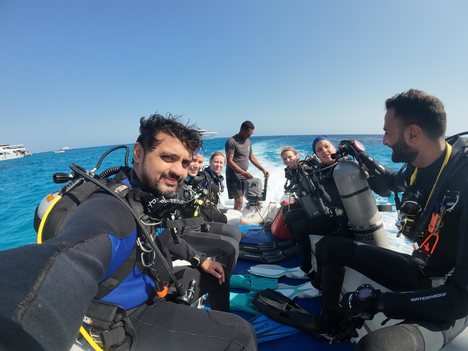 Divers sitting along the benches in full kit as the boat runs out to the site, open water beyond the rail.