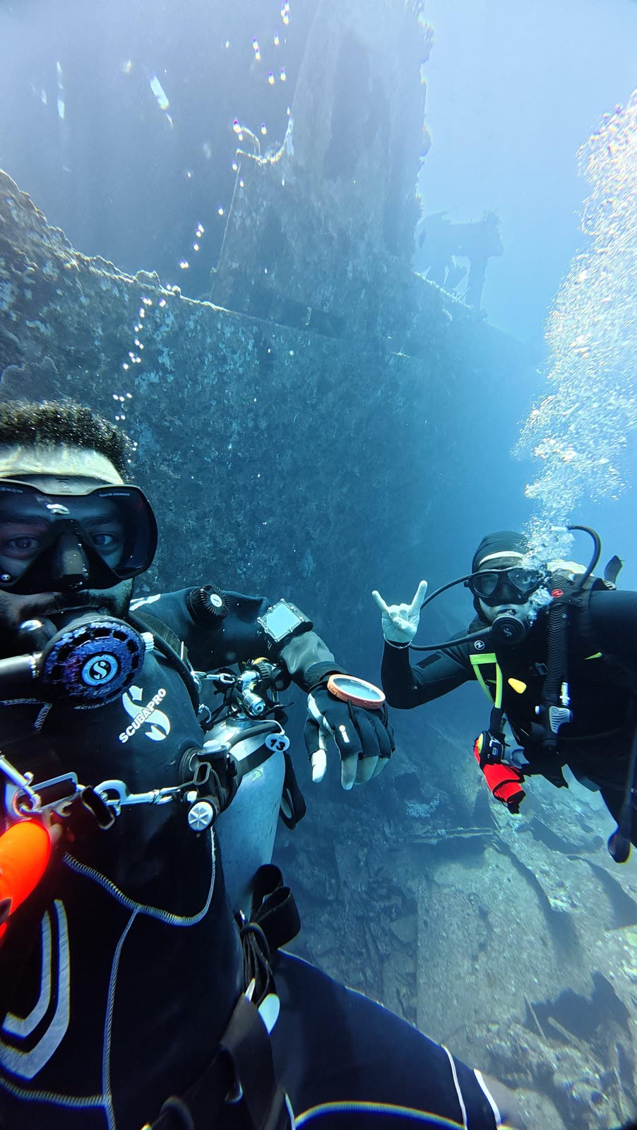 Two divers taking a selfie beside a wreck in blue water.