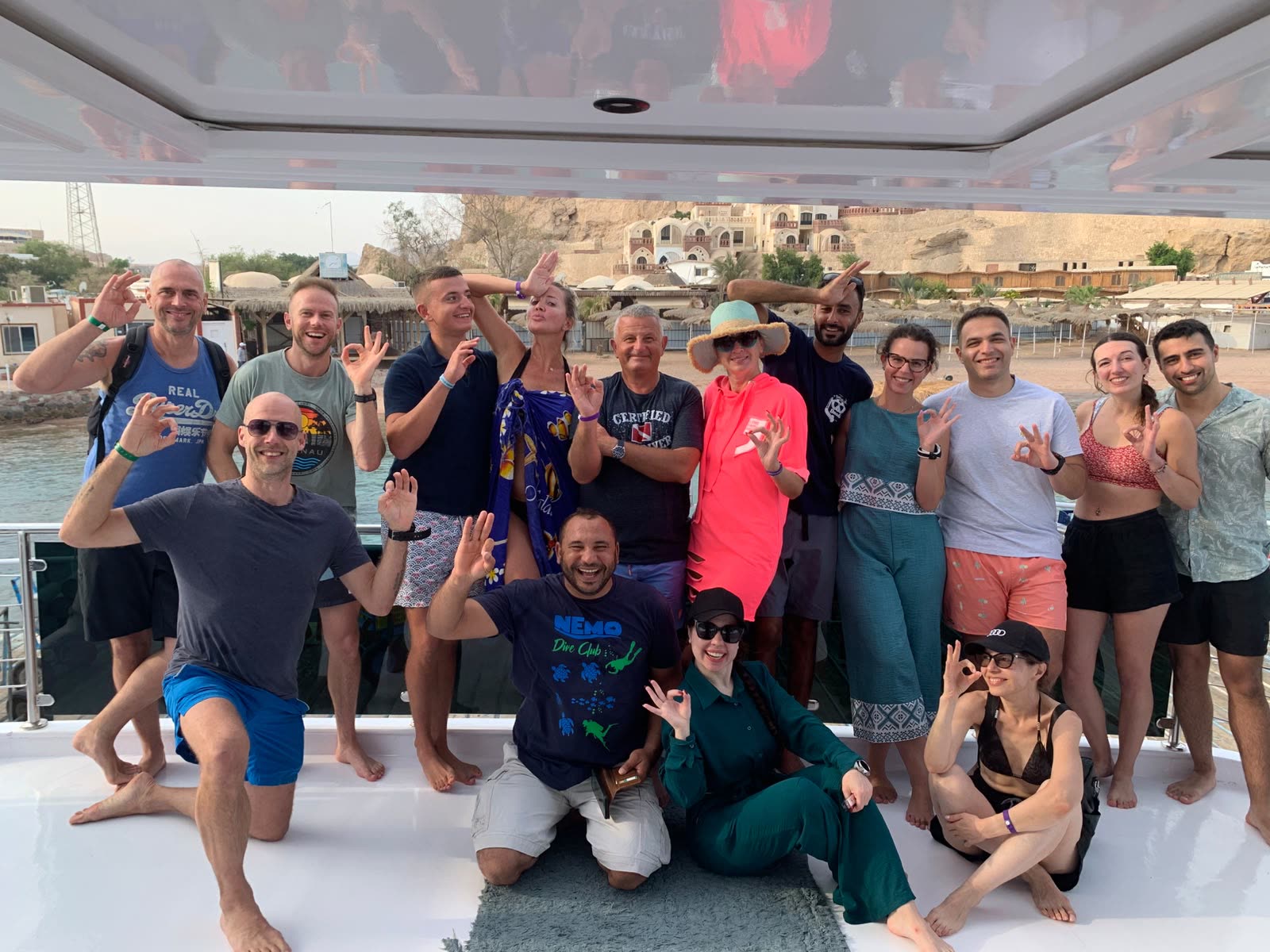 A big group of guests and crew on the boat deck, all smiling and waving.