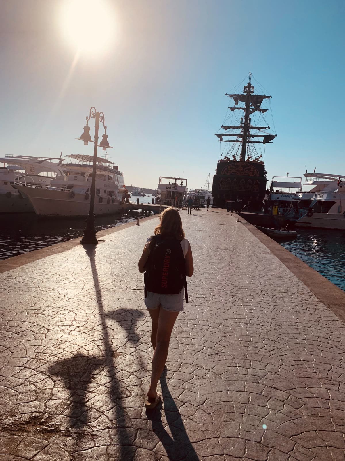 A guest walking along the marina towards the boats, a wooden sailing ship moored alongside.