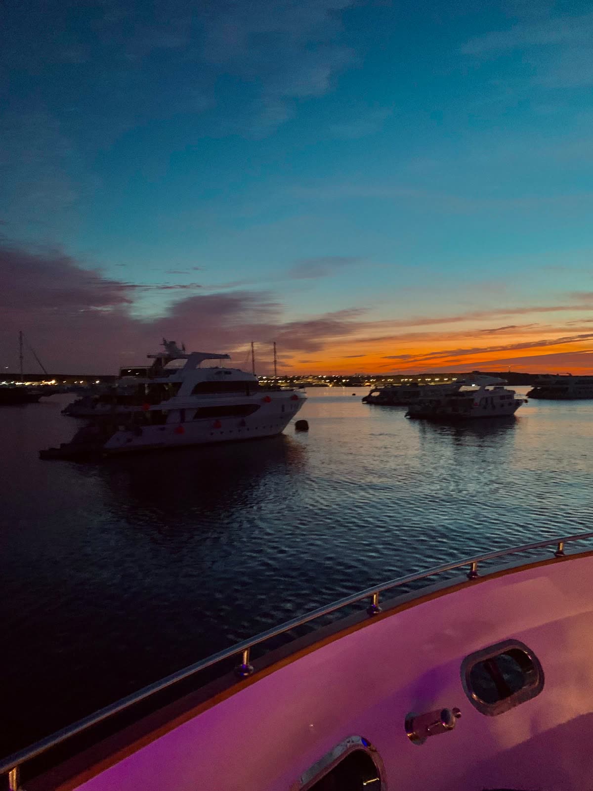 Boats at anchor at dusk, seen over the bow of the boat.