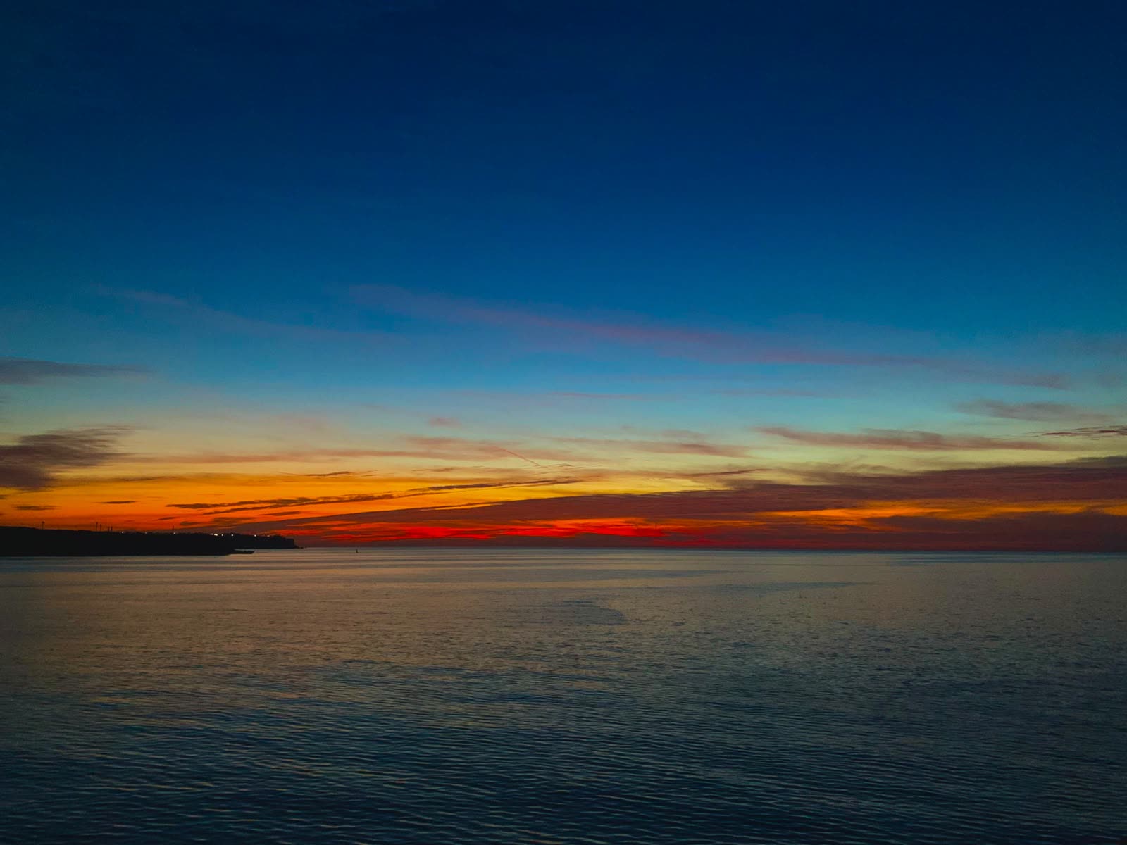 The sun just below the horizon, a band of orange over calm sea.