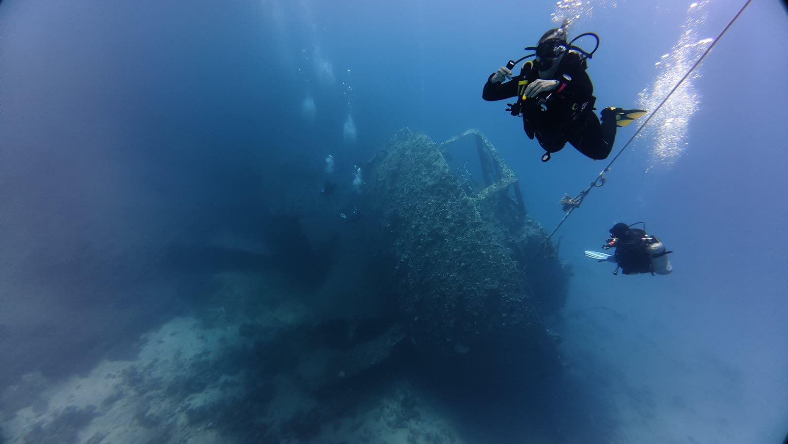 The outline of a large wreck in blue water, a diver above it.