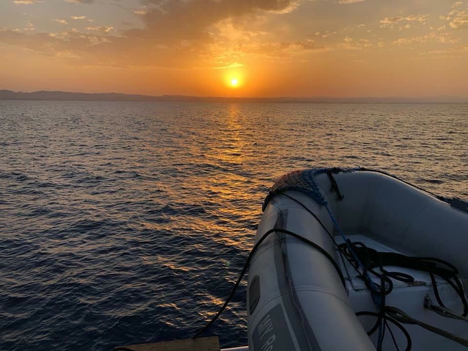 The sun low over flat water, seen from the boat with the grey inflatable tender in the foreground.