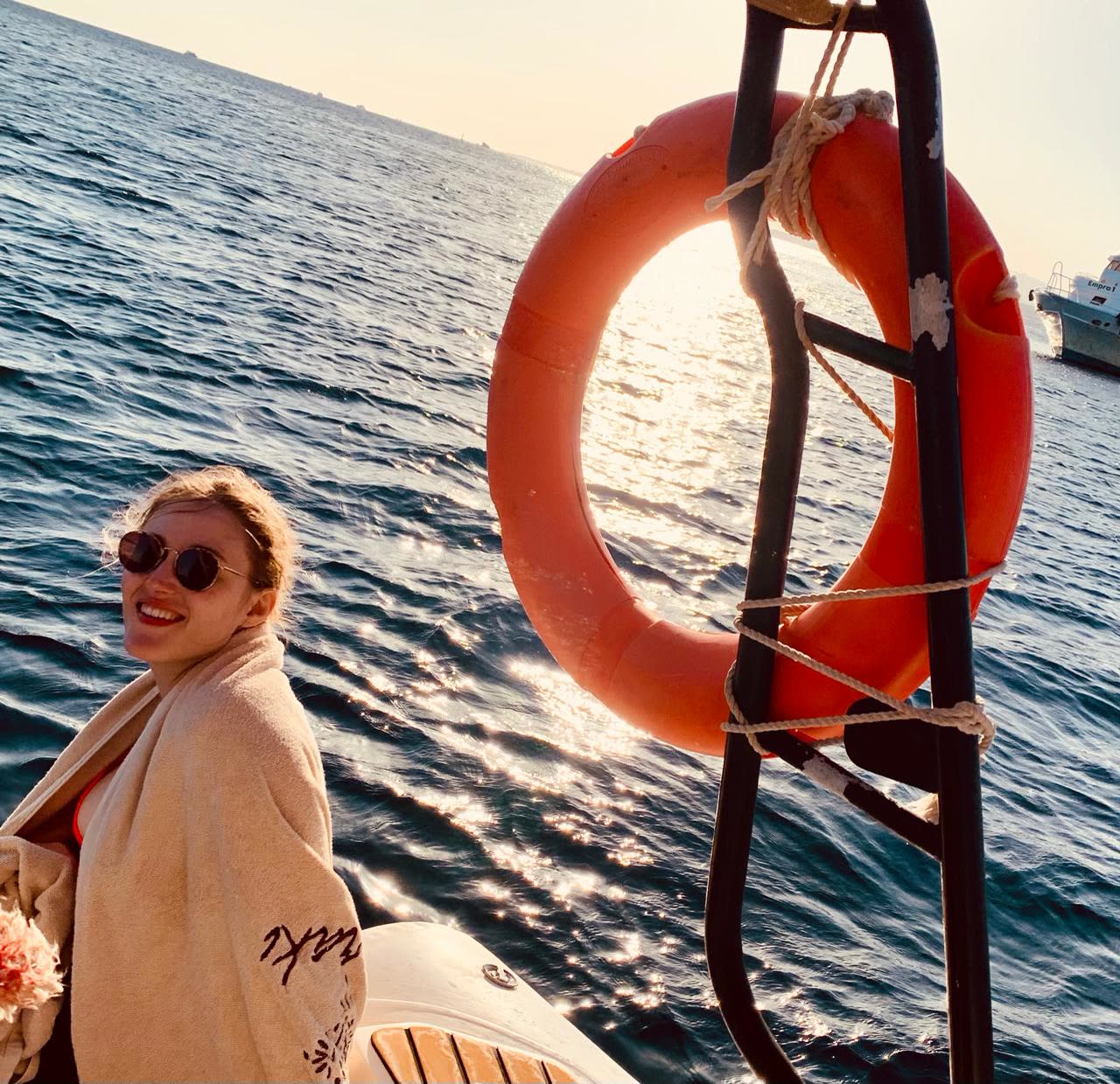 A smiling guest wrapped in a towel beside the life ring on the boat.